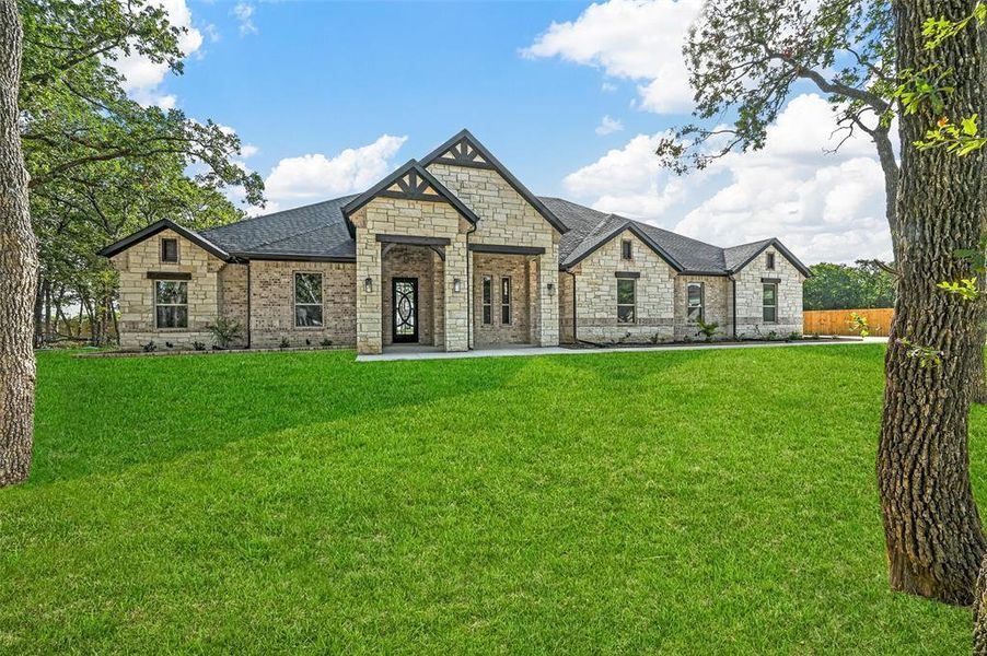 French country home with stone siding, a front yard, and a shingled roof