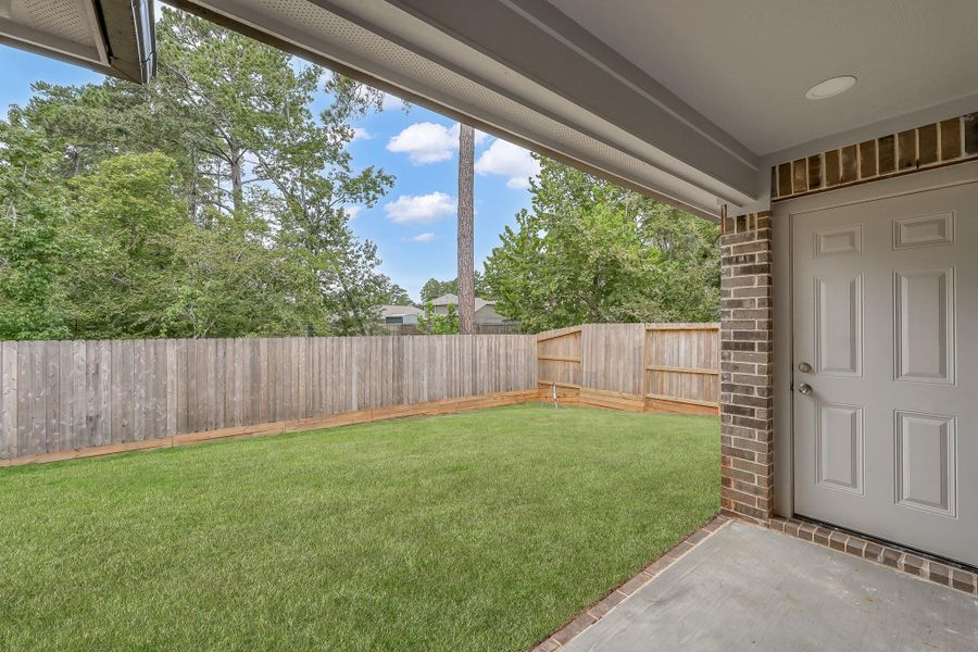 A cozy backyard with a well-maintained lawn and a tall wooden fence for privacy. The covered patio area features brick accents and a secure door, perfect for outdoor relaxation and entertainment.