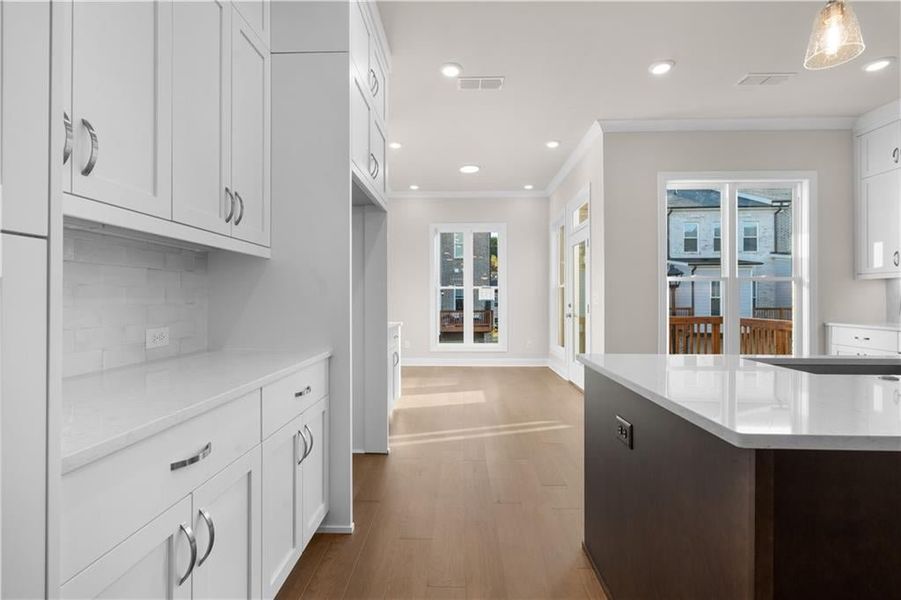 Kitchen featuring recessed lighting, light stone countertops, white cabinetry, ornamental molding, and light wood-type flooring