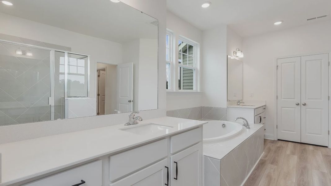 Stonehaven home plan primary bathroom with separate vanities, soaking tub, linen closet and tile shower
