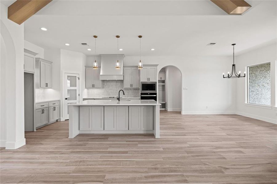 Kitchen with arched walkways, backsplash, a kitchen island with sink, decorative light fixtures, and custom exhaust hood Kitchen with arched walkways, backsplash, a kitchen island with sink, decorative light fixtures, and custom exhaust hood