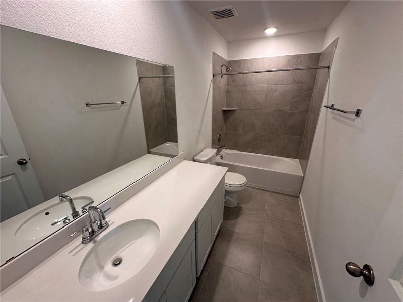Full bath featuring bathing tub / shower combination, vanity, dark tile patterned floors, and a textured wall Full bath featuring bathing tub / shower combination, vanity, dark tile patterned floors, and a textured wall