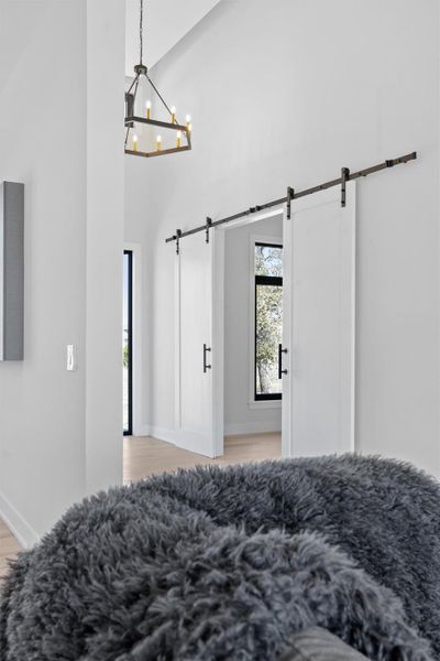 Bedroom featuring a barn door, high vaulted ceiling, light wood-style flooring, and a chandelier