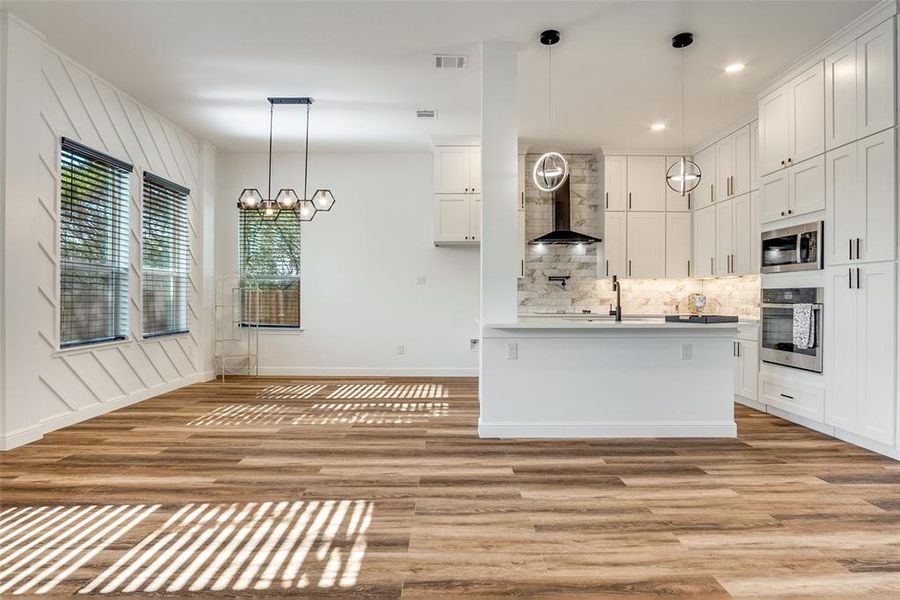 Kitchen featuring hanging light fixtures, appliances with stainless steel finishes, white cabinetry, decorative backsplash, and light wood-style flooring