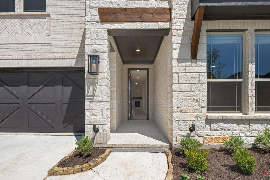 Home entrance with stone exterior, covered entryway, wood beam accents, and dark garage door nearby