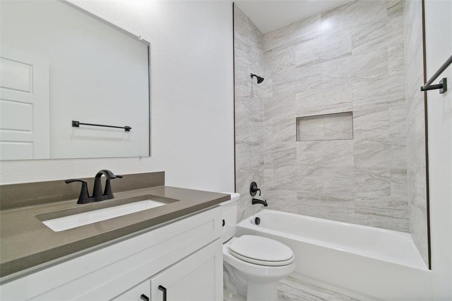 Full bathroom featuring vanity, tiled shower / bath combo, and toilet