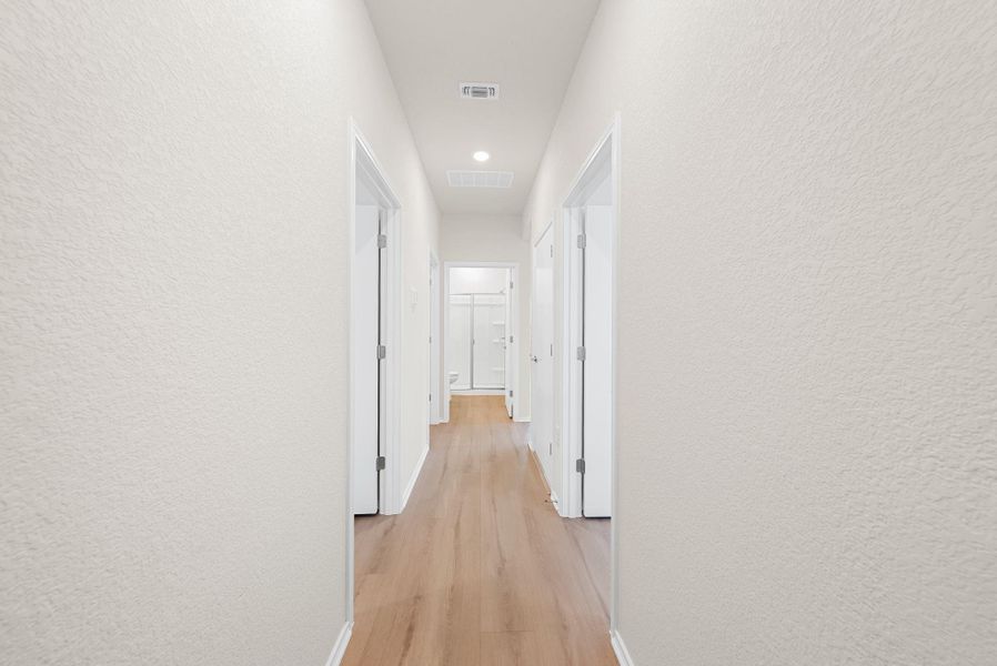A well-lit corridor with warm wood-tone flooring leads to various rooms. A well-lit corridor with warm wood-tone flooring leads to various rooms.