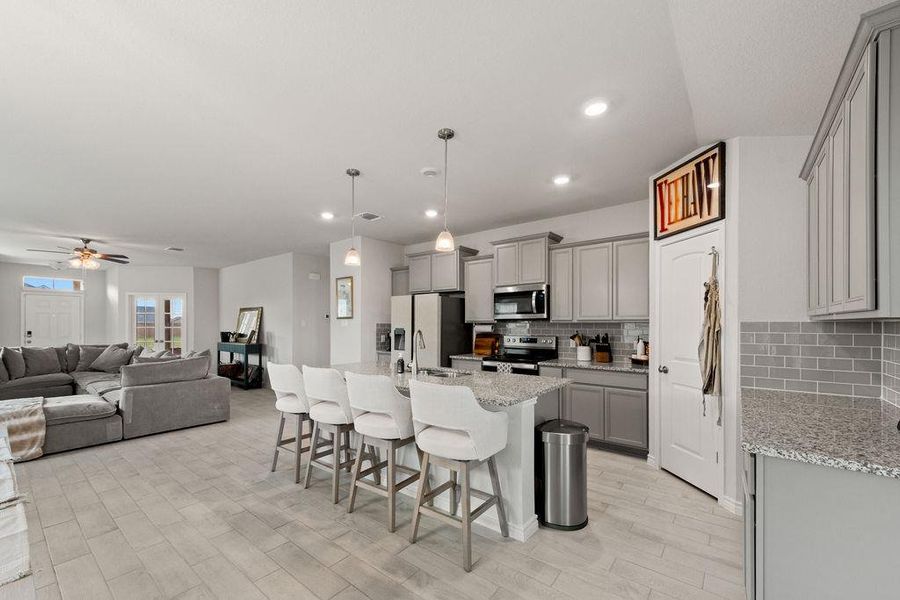 Kitchen featuring a breakfast bar area, open floor plan, tasteful backsplash, decorative light fixtures, and gray cabinetry