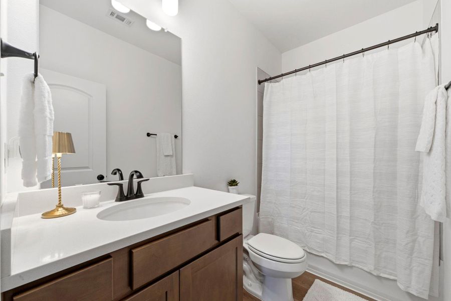 Full guest bath with quartz countertops, modern fixtures, and a tiled tub/shower combination.