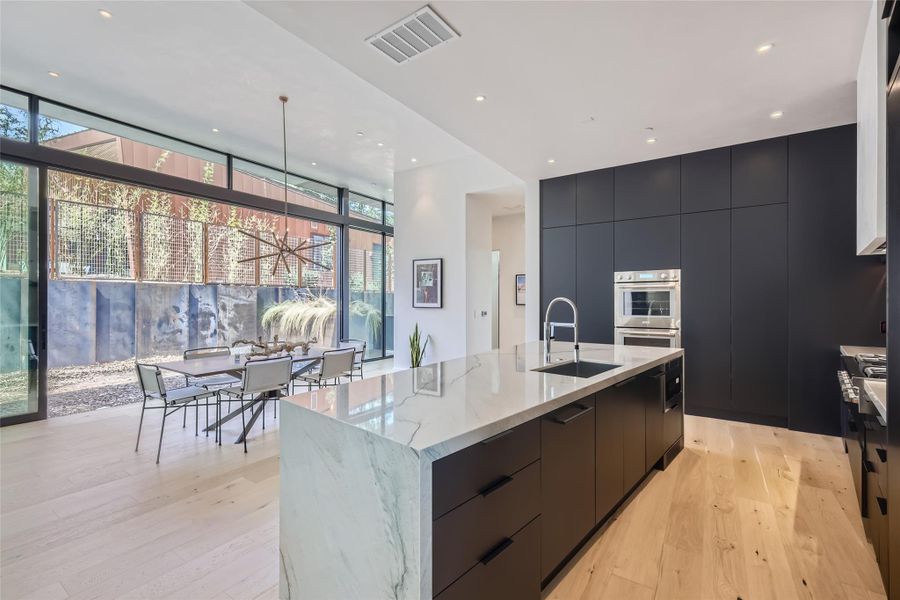A sleek, contemporary kitchen with a substantial island and integrated appliances overlooks an elegant dining area. A sleek, contemporary kitchen with a substantial island and integrated appliances overlooks an elegant dining area.