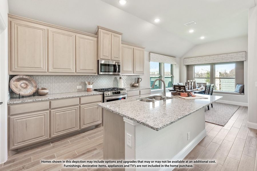 Kitchen with light wood cabinets, granite island with sink, and stainless steel appliances open to dining area