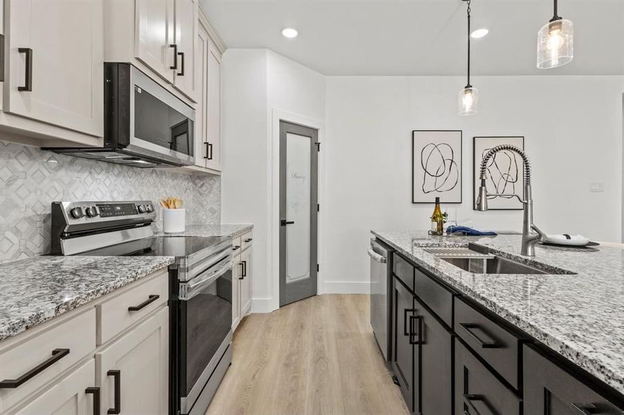 Kitchen with a sink, decorative backsplash, hanging light fixtures, appliances with stainless steel finishes, and light wood-type flooring