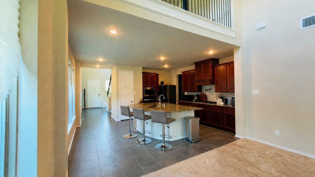 An open-concept view shows the transition from a carpeted room to a tiled kitchen and hallway.**This room has been virtually staged.