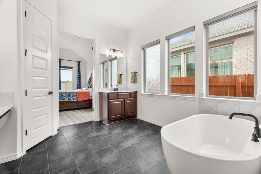 A well-appointed primary bathroom featuring a freestanding tub and dark tile flooring. A well-appointed primary bathroom featuring a freestanding tub and dark tile flooring.