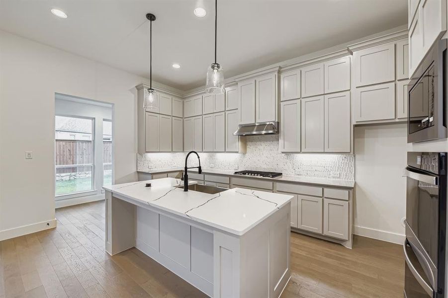 Kitchen featuring decorative backsplash, a center island with sink, light wood finished floors, hanging light fixtures, and recessed lighting