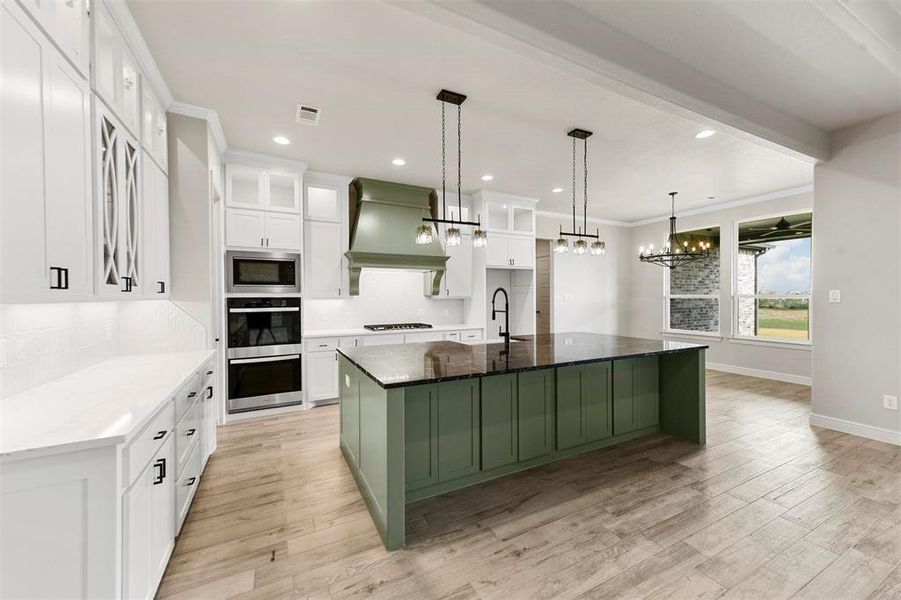 Kitchen featuring premium range hood, a large island with sink, dark stone countertops, white cabinets, and light hardwood / wood-style floors