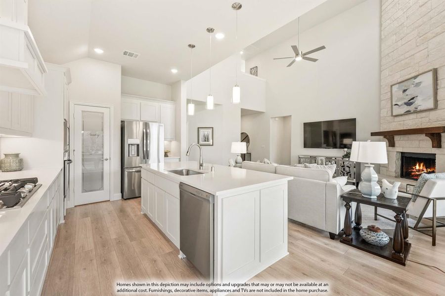 Open-concept kitchen with white island and cabinets flowing into living room with stone fireplace and high ceilings