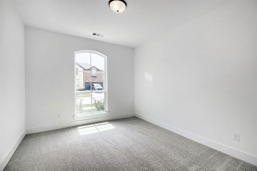 Bright room featuring an arched window, light gray carpet flooring, white walls, white baseboards, and a flush mount ceiling light fixture Bright room featuring an arched window, light gray carpet flooring, white walls, white baseboards, and a flush mount ceiling light fixture
