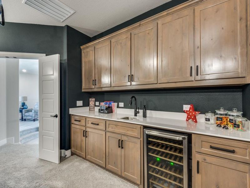 Bar with light carpet, a textured ceiling, sink, and beverage cooler