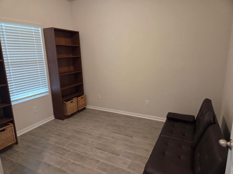 Spacious room featuring wood-look tile flooring, neutral wall paint, and a window with horizontal blinds