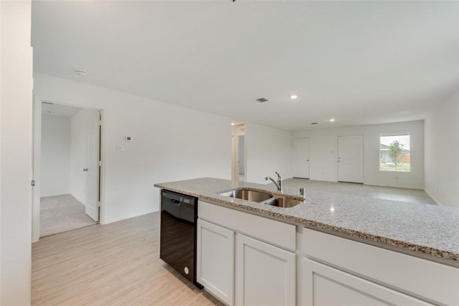 Kitchen with white cabinetry, dishwasher, sink, light stone counters, and light hardwood / wood-style floors