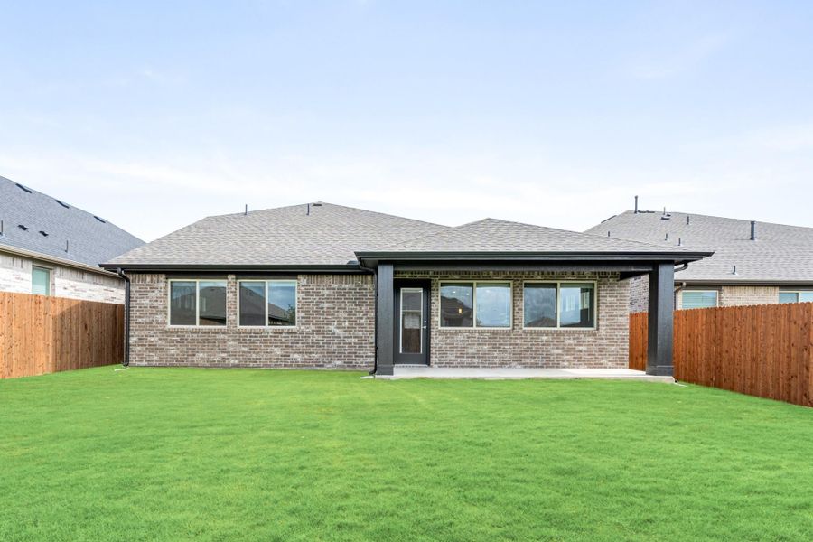 Rear view of single-story brick home with large green backyard and wood privacy fence