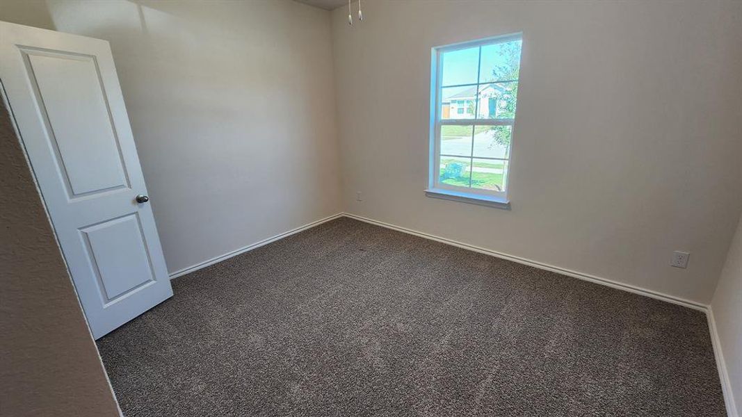 Carpeted room featuring a single window with white trim, a six-panel interior door, and white baseboards Carpeted room featuring a single window with white trim, a six-panel interior door, and white baseboards