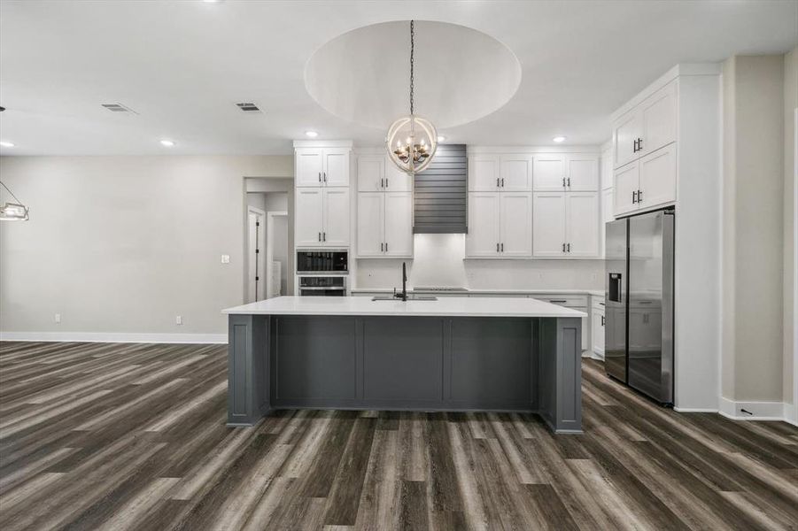 Kitchen featuring dark hardwood / wood-style flooring, pendant lighting, stainless steel refrigerator with ice dispenser, and white cabinets