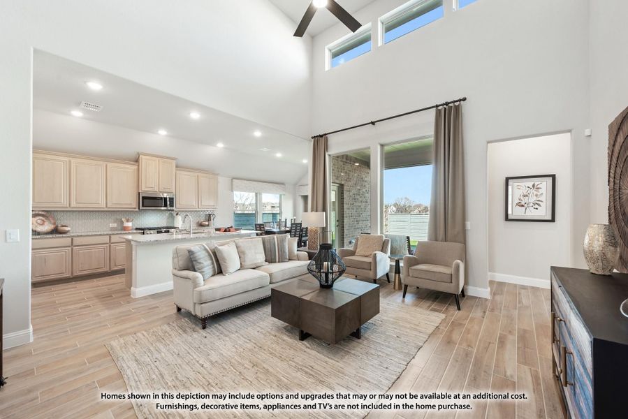 Open-concept living room with vaulted ceiling, wood-look floors, and kitchen visible in background
