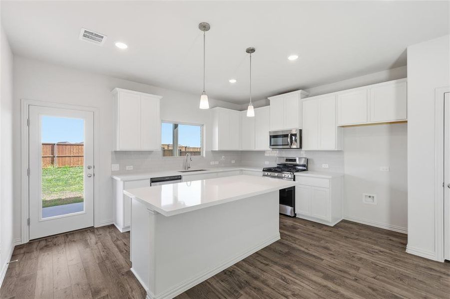 Contemporary kitchen featuring white cabinetry, stainless steel appliances, a center island with pendant lighting, and wood-finish flooring