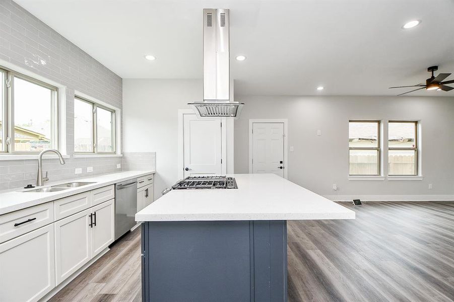 This is a spacious, modern kitchen with white cabinetry, a contrasting blue island, stainless steel appliances, and sleek gray flooring. It features ample natural light and a contemporary design.