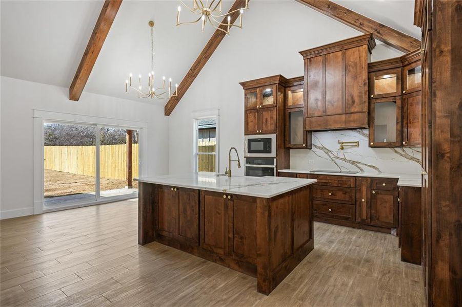 Kitchen featuring a chandelier, decorative backsplash, glass fronted cabinets, vaulted ceiling, and light stone counters