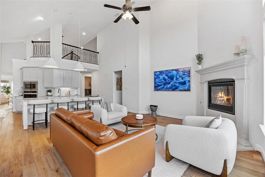 Living room featuring baseboards, a ceiling fan, high vaulted ceiling, and light wood-style flooring
