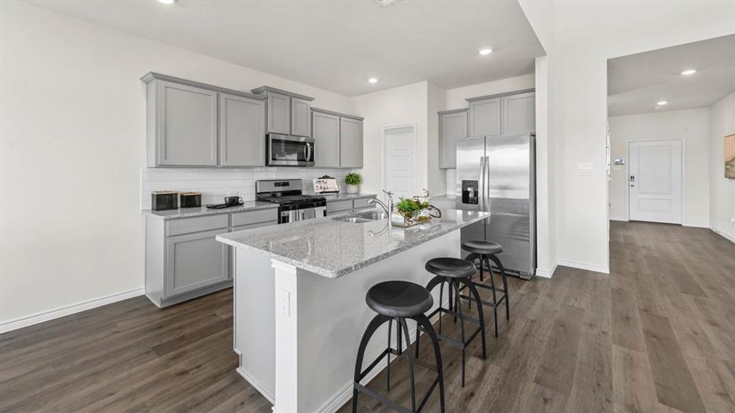 Kitchen featuring a central island with a sink, stainless steel appliances, light gray cabinetry, and white subway tile backsplash