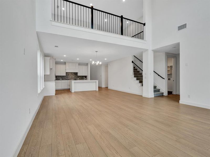 Unfurnished living room with a notable chandelier, light hardwood / wood-style flooring, and a towering ceiling