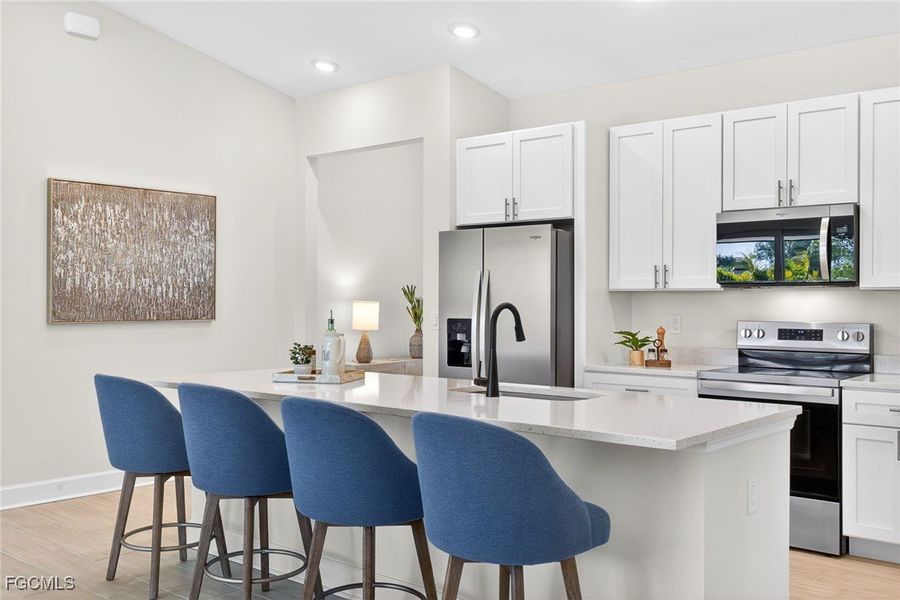 Kitchen featuring appliances with stainless steel finishes, white cabinetry, light wood finished floors, light stone counters, and recessed lighting