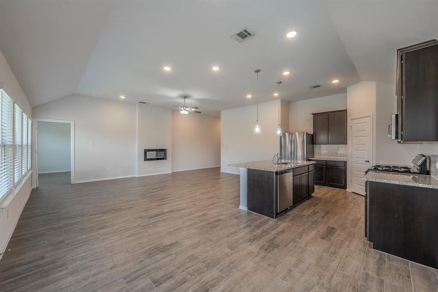 Kitchen featuring lofted ceiling, open floor plan, dark brown cabinets, an island with sink, and light stone counters Kitchen featuring lofted ceiling, open floor plan, dark brown cabinets, an island with sink, and light stone counters