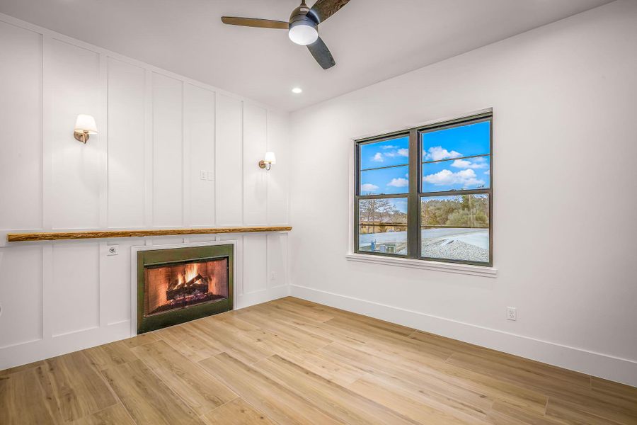 Unfurnished living room with a decorative wall, light wood-style flooring, ceiling fan, a warm lit fireplace, and baseboards