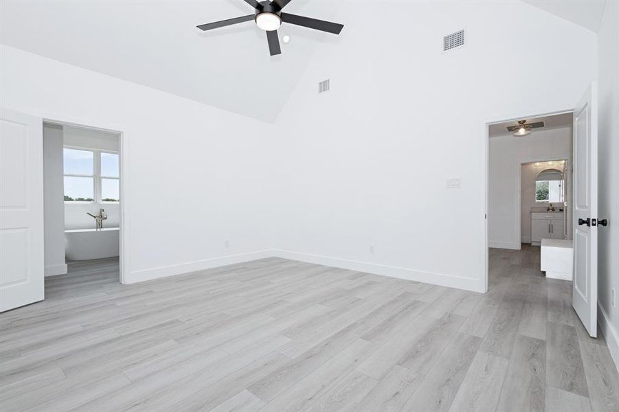 Unfurnished bedroom featuring high vaulted ceiling, multiple windows, light wood-type flooring, and a ceiling fan