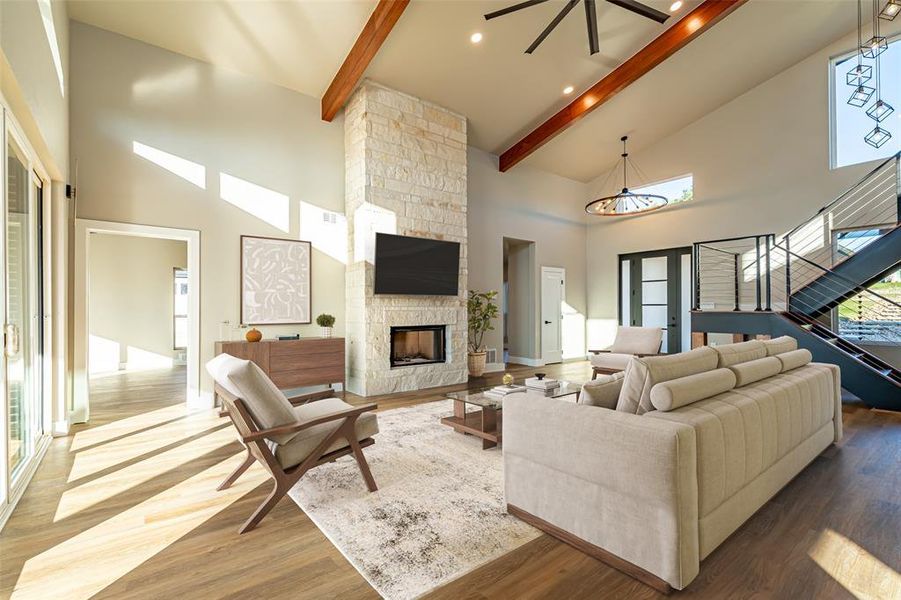 Living room with high vaulted ceiling, a stone fireplace, beam ceiling, wood finished floors, and stairs Living room with high vaulted ceiling, a stone fireplace, beam ceiling, wood finished floors, and stairs