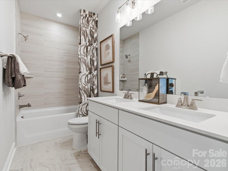 Dual vanity secondary bathroom with tiled walls above the tub