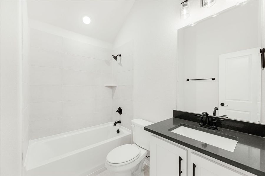 Bathroom with white tub-shower combo, dark countertop vanity, and black fixtures