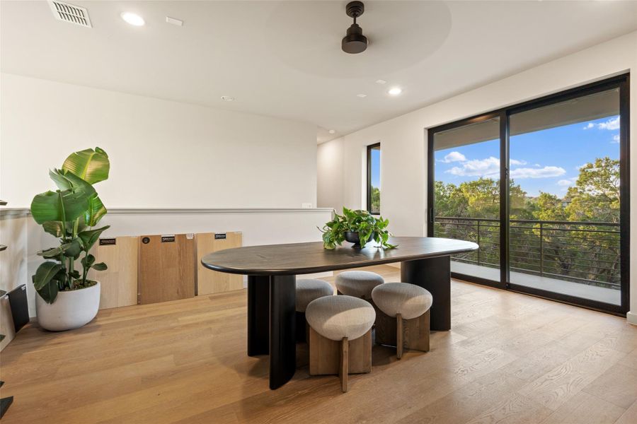 A spacious dining area featuring elegant hardwood flooring and a serene natural view from the balcony.