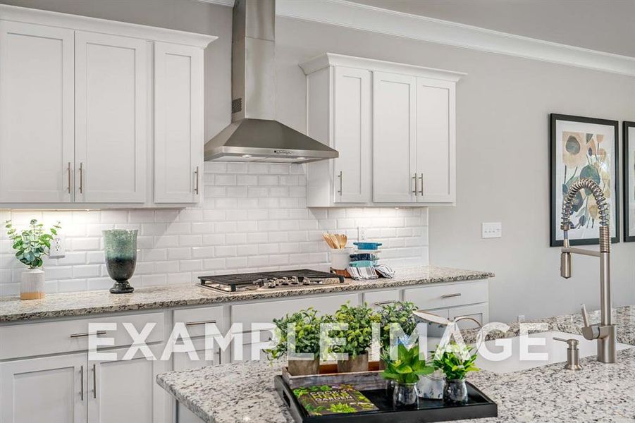 Kitchen featuring white cabinets, stainless steel gas stovetop, decorative backsplash, and wall chimney range hood