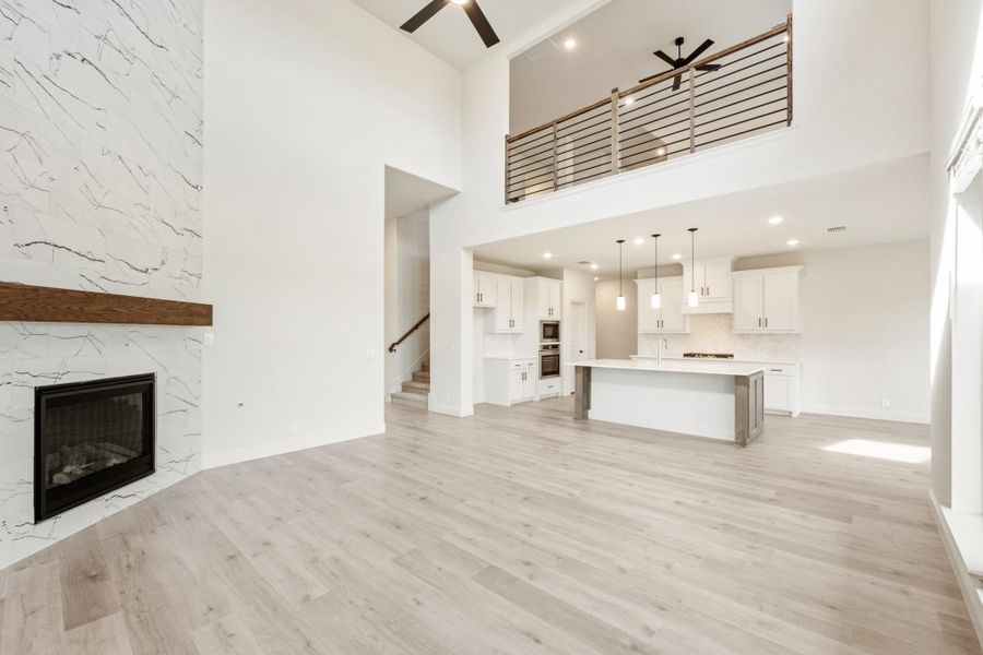 Open-concept living area with two-story ceiling, marble fireplace, and kitchen island visible in background Open-concept living area with two-story ceiling, marble fireplace, and kitchen island visible in background