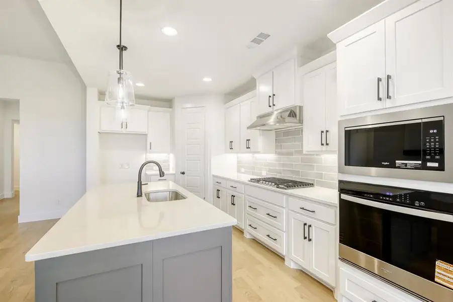 Dual tone kitchen featuring stainless steel appliances, a center island with sink, light wood-style floors, light stone countertops, and two tone cabinetry