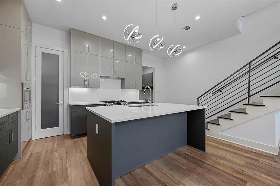 Kitchen featuring pendant lighting, sink, a center island with sink, gray cabinets, and light hardwood / wood-style floors