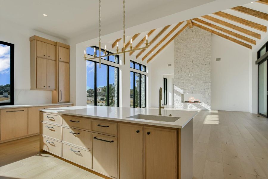 Kitchen with light wood finish cabinetry, light wood-style flooring, a fireplace, light stone countertops, and open floor plan