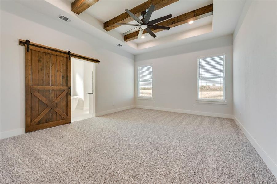 Carpeted empty room featuring a tray ceiling, a barn door, ceiling fan, and beamed ceiling