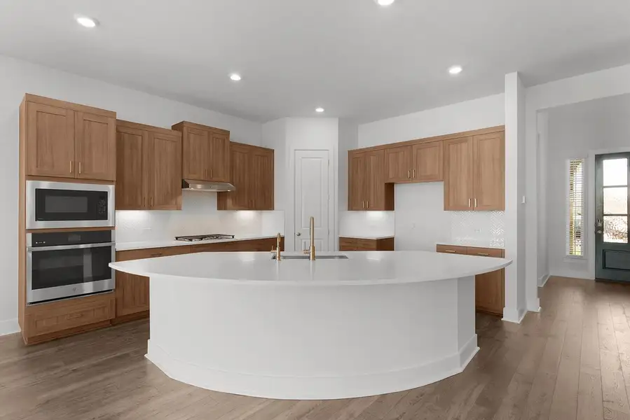 A well-lit kitchen with sleek wooden cabinetry and a large, curved central island.